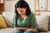 Woman experiencing stomach pain, a common symptom of IBS, sitting on a sofa and holding her abdomen